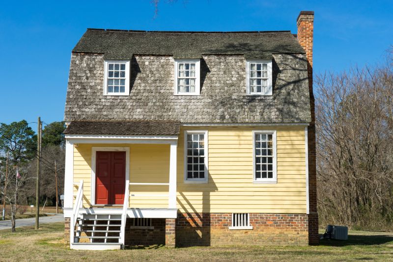 photo of historic home, yellow, second story dormers, red door.